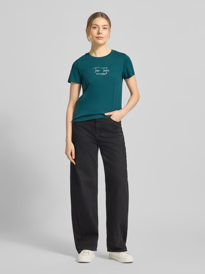 Modelka nosi Regular Fit T-Shirt aus Bio-Baumwoll-Mix von Tom Tailor, unikatowy kolor, napis z logo, okrągły dekolt, krótki rękaw, przód, pełny widok ciała.