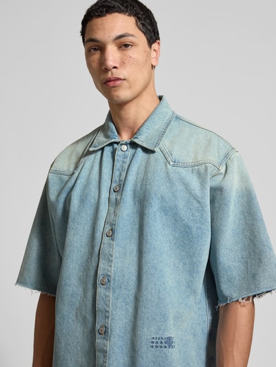 Männermodel trägt Relaxed Fit Jeanshemd mit Logo-Stitching von MM6 Maison Margiela aus reiner Baumwolle in hellem Blau, Nahaufnahme Oberkörper.