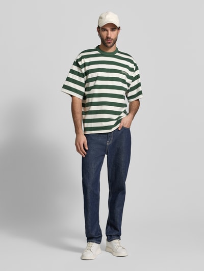 Männermodel trägt Relaxed Fit T-Shirt mit Logo-Stitching Modell 'Beam' von Woodbird aus reiner Baumwolle mit Rundhalsausschnitt, grün-weiß gestreift, Herren T-Shirt, Ganzkörperansicht von vorne.