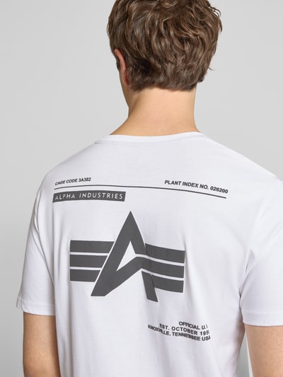Männermodel trägt T-Shirt mit Label-Patch von Alpha Industries in Weiß und Schwarz, Reine Baumwolle, Gerader-Schnitt, Ganzkörperansicht Rückansicht.
