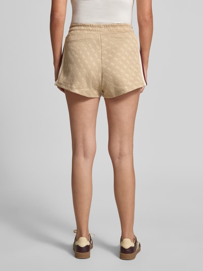 Frauenmodel trägt Shorts mit Allover-Logo-Print Modell 'Jacquard' von Guess Activewear in Beige, ausgestellte Passform, Baumwoll-Mix, elastischer Bund, Eingrifftaschen, Ganzkörperansicht Rückansicht.