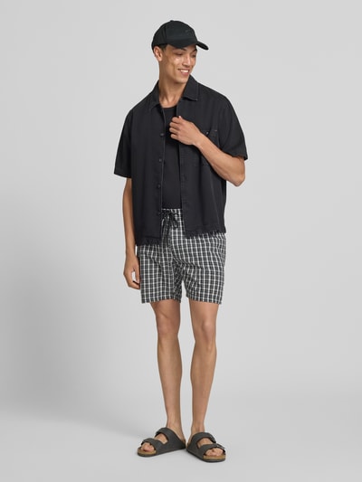 Männermodel trägt Shorts mit elastischem Bund Modell 'SLADE' von Redefined Rebel aus Reine Baumwolle, Regular-Fit, Ganzkörperansicht von vorne, kariertes Muster, Bundweite 37 cm, Innenbeinlänge 18 cm, Kordelzug.