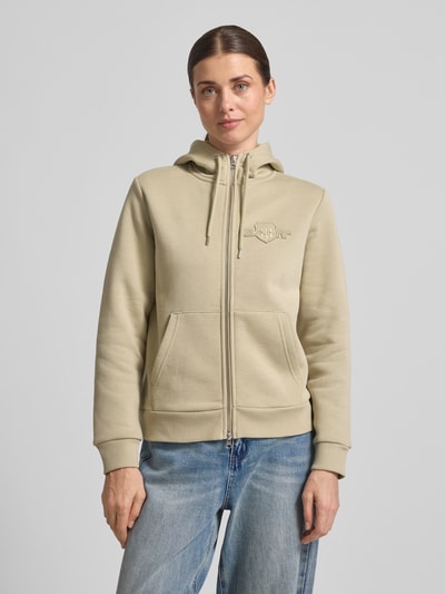 Frauenmodel trägt Sweatjacke mit Zweiwege-Reißverschluss und Label-Stitching von Gant im sandfarbenen Baumwoll-Mix, Känguru-Tasche, Kapuze, Regular Fit, Ganzkörperansicht von vorne.