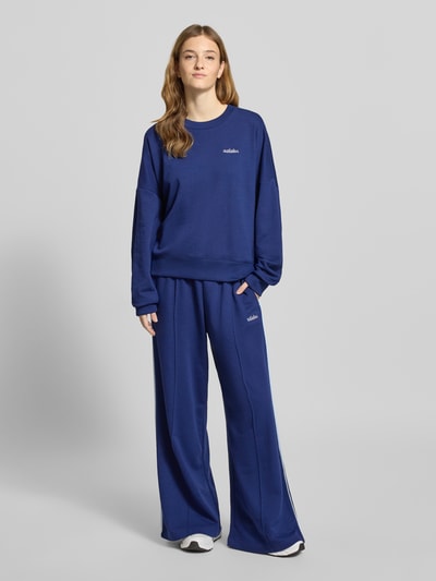 Modelka nosi Sweatshirt mit Label-Stitching von adidas Sportswear, bawełniany miks z domieszką rayonu, luźny krój, ściągacze, okrągły dekolt, granatowy kolor, widok całej sylwetki z przodu