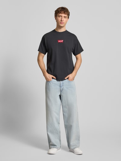 Męski model nosi T-shirt mit Label-Detail von LEVI'S®, bawełna, krój regular fit, prążkowany okrągły dekolt, długość tyłu 68 cm, Ganzkörperansicht von vorne.