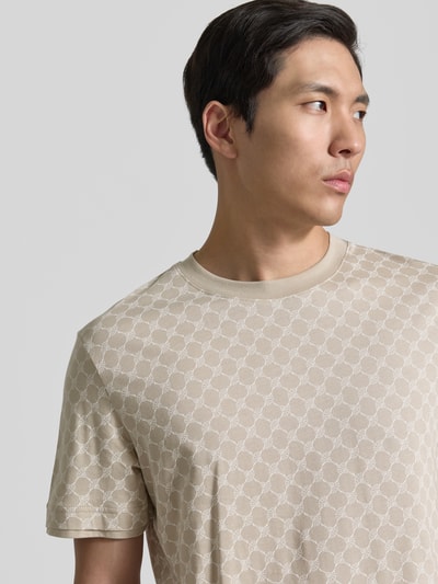 Männermodel trägt T-Shirt mit Logo-Muster und Rundhalsausschnitt von JOOP! Collection aus Baumwoll-Lyocell-Mix, Regular-Fit, Beige, Nahaufnahme Oberkörper.