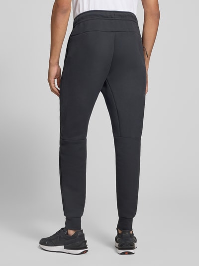 Männermodel trägt Slim Fit Sweathose aus Baumwoll-Mix von Nike in Dunkelgrau mit glatter Textur, Ganzkörperansicht Rückansicht. Herren Sweathose von Nike