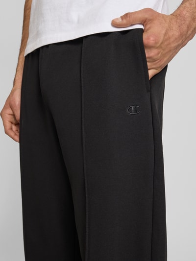 Männermodel trägt schwarze Sweatpants mit Längsnähten und Label-Stitching von CHAMPION aus Baumwoll-Mix, Nahaufnahme Oberkörper.
