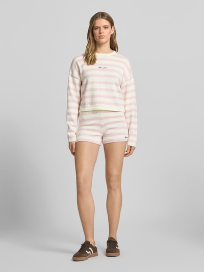 Frauenmodel trägt Boxy Fit Strickpullover mit Streifenmuster und Label-Stitching von Guess Jeans in Reine Baumwolle, Rundhalsausschnitt, Ganzkörperansicht von vorne.