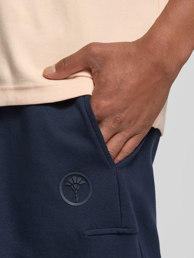 Männermodel trägt Shorts mit Eingrifftaschen Modell 'Joseignacio' von JOOP! Collection in Dunkelblau, Nahaufnahme Hüftbereich, Baumwoll-Mix mit Label-Patch und sichtbarer Tasche.