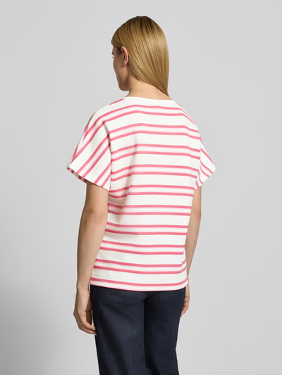 Kobieta nosi damski t-shirt z mieszanki materiałów z domieszką modalu Soyaconcept, model 'BARNI', okrągły dekolt, krój relaxed fit, białe tło z różowymi i czerwonymi paskami, widok całej sylwetki od tyłu.