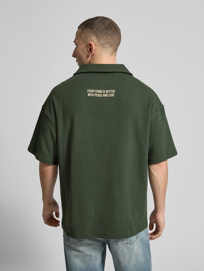 Männermodel trägt Wide Fit Poloshirt mit Label-Print von ANOTHER COTTON LAB in Dunkelgrün, Baumwoll-Mix, Rückenansicht, Ganzkörperansicht Rückansicht.