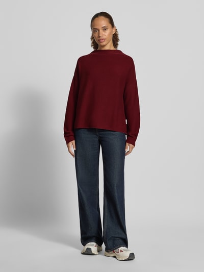 Frauenmodel trägt Loose Fit Pullover aus reiner Baumwolle Modell 'MERINAA' von ARMEDANGELS in Dunkelrot zu blauer Jeans, Ganzkörperansicht von vorne. Damen Pullover von ARMEDANGELS.