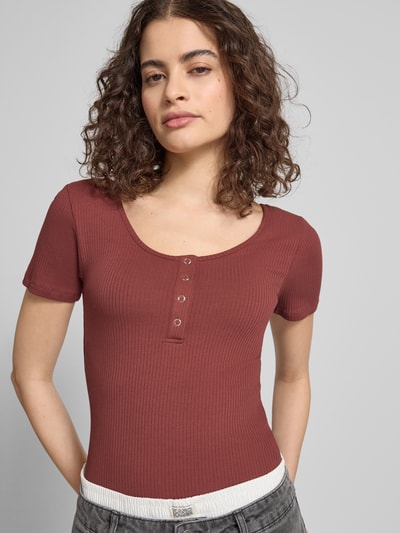 Modelka kobieca nosi Slim Fit T-Shirt aus Baumwoll-Mix Modell 'KITTE' od Pieces, bawełna, gładka, krótki rękaw, krój slim fit, rib, u-neck, Henley. Zbliżenie na górną część ciała.