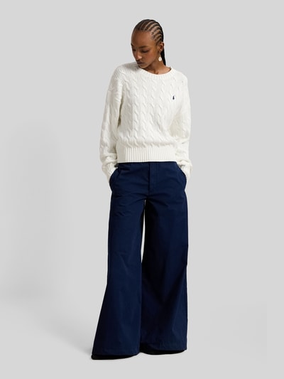 Modelka nosi Regular Fit Strickpullover aus reiner Baumwolle od Polo Ralph Lauren, kremowy, gładki, dzianina, splot warkoczowy, logo, długi rękaw, wykończenia ściągaczem, krój regular fit, widok całej sylwetki z przodu.
