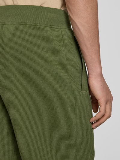 Männermodel trägt Straight Fit Shorts mit Strukturmuster von G-Star Raw in Olivgrün, Elastischer-Material-Mix mit Baumwoll-Anteil, Logo-Detail, Nahaufnahme Rückansicht.