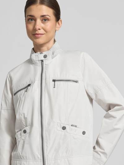 Frauenmodel trägt Jacke mit Zweiwege-Reißverschluss von Amber & June in Hellgrau mit Stehkragen, Brusttaschen, Nahaufnahme Oberkörper.