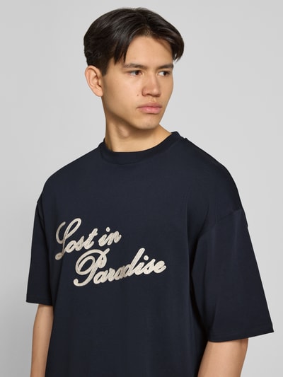 Männermodel trägt T-Shirt mit Logo- und Statement-Stitching von REVIEW aus Reine Baumwolle, Gerader-Schnitt, Gerippter Rundhalsausschnitt, Nahaufnahme Oberkörper.