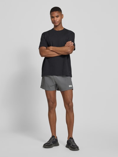 Männermodel trägt Relaxed Fit Shorts mit integriertem Slip von EA7 Emporio Armani mit Strukturmuster, Logo-Patch, Elastischer-Material-Mix, Elastischer Bund, Bundweite 41 cm, Innenbeinlänge 10 cm in Grau und Schwarz; Ganzkörperansicht von vorne.