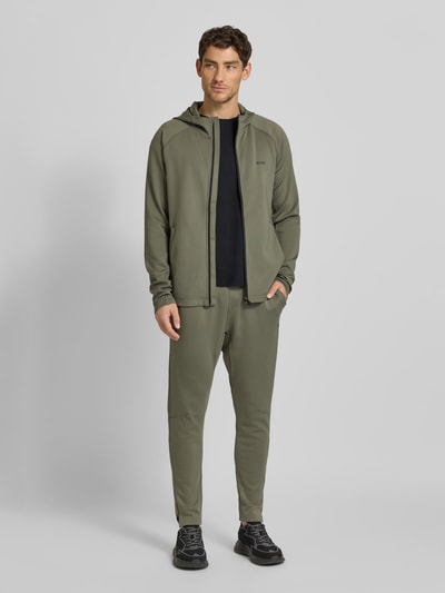 Männermodel trägt Regular Fit Trainingsjacke aus schnell trocknendem Gewebe Modell 'SICON ACTIVE' von BOSS Green, Optik: Unifarben, mit Kapuze, Reißverschluss, Label-Print, Reißverschlusstaschen, Daumenschlaufen, Ganzkörperansicht von vorne.