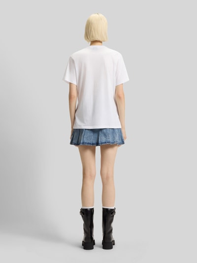 Frauenmodel trägt weißes Relaxed Fit T-Shirt aus reiner Baumwolle Modell 'VINTAGE TEE_B_1' von Hugo Blue, unifarben, Rundhals, Label Patch, kurzarm, kombiniert mit Jeansrock und schwarzen Stiefeln, Ganzkörperansicht Rückansicht.
