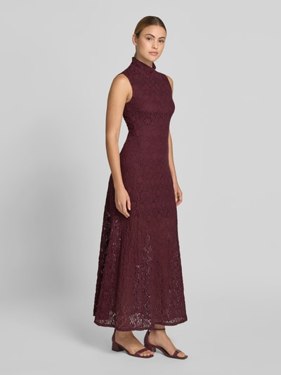 Frauenmodel trägt Maxikleid mit Allover-Spitzenbesatz von ROTATE aus Elastischer-Material-Mix mit Baumwoll-Anteil, Slim-Fit, Stehkragen, ärmelloses Design, Farbe Bordeaux, florale Spitze als Textur, Gesamtlänge bei Größe 36: 144 cm, Brustweite: 44 cm, Ganzkörperansicht von vorne.