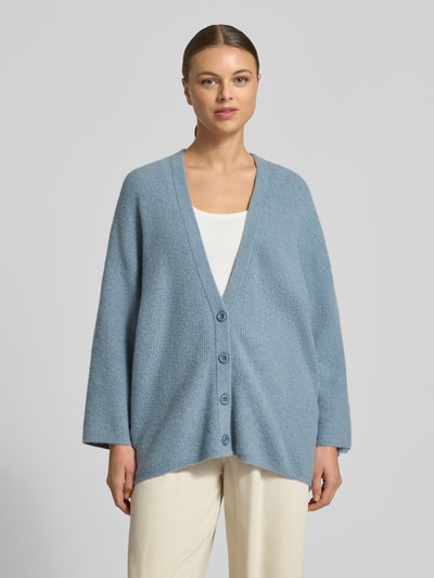 Frauenmodel trägt Relaxed Fit Cardigan mit Woll-Anteil Modell 'Damsville' von American Vintage in Hellblau, Strick-Optik, V-Ausschnitt, Knopfleiste, Ganzkörperansicht von vorne.
