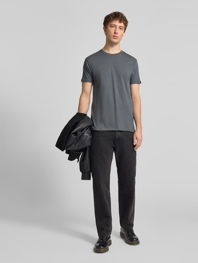 Męski model nosi T-Shirt aus Baumwolle od Alpha Industries, prosty krój, okrągły dekolt, detale z logo, kolor szary, długość tyłu 68 cm, rozmiar M, całopostaciowy widok z przodu.