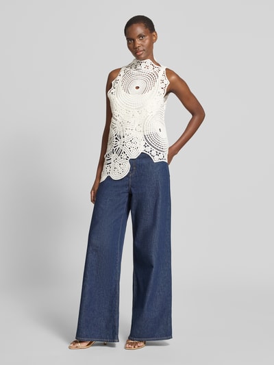 Frauenmodel trägt Stricktop aus Häkelspitze Modell 'CRYSTAL' von Copenhagen Muse in Reine Baumwolle, Asymmetrischer-Schnitt, blickdichtes Untertop, dunkle Jeans, Ganzkörperansicht von vorne.