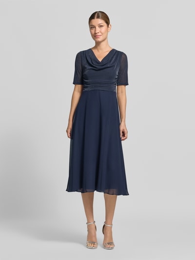 Kobiece modelka nosi Fit and Flare Cocktailkleid mit Wasserfallausschnitt od Vera Mont, granatowa, lekko połyskująca góra, rozkloszowany dół, sukienka koktajlowa, widok całej sylwetki z przodu.
