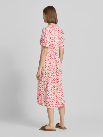 Frauenmodel trägt A-Linien Midikleid aus reiner Viskose Modell 'TALA' von Pieces, Allover-Muster in Rosa und Rot, Ganzkörperansicht Rückansicht.