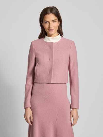 Modelka kobieca nosi Boxy Fit Kurzblazer aus reiner Schurwolle Modell 'JICENA' od BOSS w jednolitym, różowym kolorze, długi rękaw, okrągły dekolt, boczne kieszenie, materiał z czystej wełny, widoczna faktura, zdjęcie całej sylwetki od przodu.
