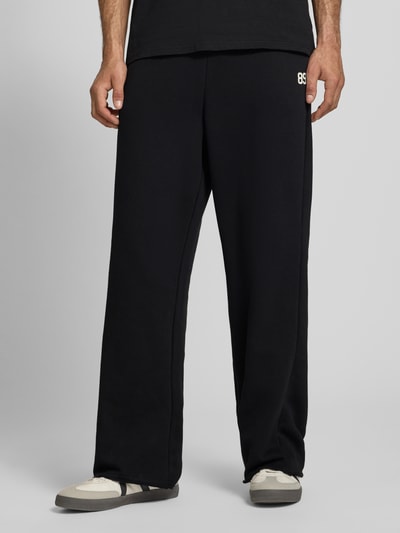 Männermodel trägt Straight Fit Sweatpants mit Gesäßtasche von KARL KANI aus Baumwoll-Mix in Schwarz, Ganzkörperansicht von vorne.