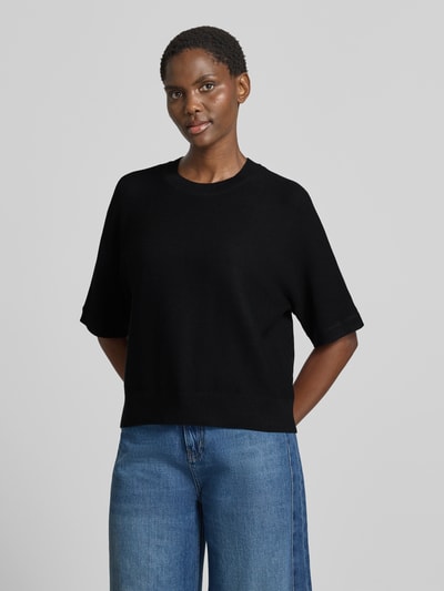 Frauenmodel trägt Relaxed Fit Pullover aus Viskose-Mix Modell 'Thamira' von MSCH Copenhagen, Schwarz, Strickoptik, Halbarm, Ganzkörperansicht von vorne.