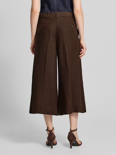 Frauenmodel trägt Loose Fit Leinenhose mit elastischem Bund Modell 'MELLI' von Brax in dunkelbraun, unifarben, cropped Länge, reine Leinenstruktur, angedeutete Gesäßtaschen, Ganzkörperansicht Rückansicht.