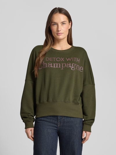Kobiece modelka nosi Oversized Sweatshirt aus reiner Baumwolle od miss goodlife w kolorze khaki, z nadrukiem z napisem, elastyczne wykończenia, okrągły dekolt, krój oversized, przód, widok na cały korpus.