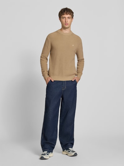 Männermodel trägt Slim Fit Pullover aus reiner Baumwolle in Strick-Optik von Replay in Beige, kombiniert mit blauer Jeans, Ganzkörperansicht von vorne.