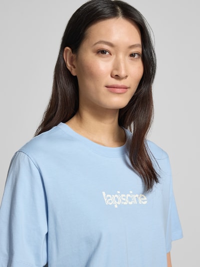 Modelka kobieca nosi Regular Fit T-Shirt aus reiner Baumwolle Modell 'MACY' od Selected Femme w jednolitym jasnoniebieskim kolorze, napis z przodu, okrągły dekolt, krótki rękaw, materiał jersey, przód ujęcie zbliżeniowe na górną część ciała.
