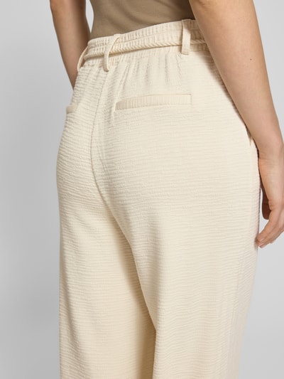 Männermodel trägt spodnie materiałowe Wide Fit Stoffhose aus Viskose-Mix Modell 'Lumina' von ICHI w kolorze kremowym, fakturowany wzór, kieszeń z tyłu, odpinany pasek z materiału, mieszanka wiskozy, szerokość w rozmiarze S: 39 cm, długość wewnętrzna nogawki: 72 cm, detaliczny widok z tyłu.