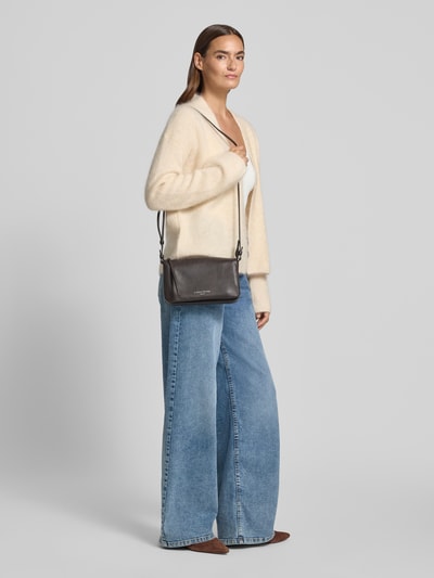 Frauenmodel trägt Crossbody Bag aus Echtleder Modell 'Nina' von LIEBESKIND BERLIN in Dunkelbraun mit Logo-Detail; Ganzkörperansicht von vorne. Breite 24 cm, Länge 15 cm, Tiefe 6 cm, Länge Schulterriemen 120 cm, geteiltes Hauptfach mit Reißverschluss, schmaler Schulterriemen.
