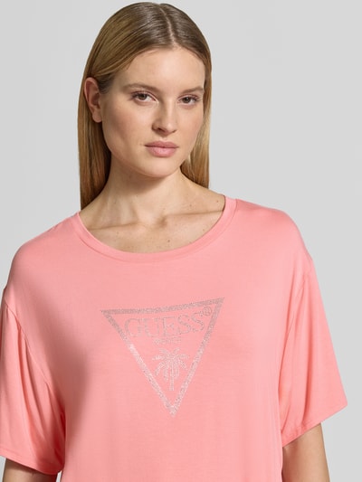 Kobiece model nosi T-Shirt mit Logo-Print Modell 'COULISSE' von Guess z mieszanki wiskozy, luźny krój, okrągły dekolt, nadruk z logo, tunel, długość tyłu w rozmiarze S: 70 cm, zbliżenie na górną część ciała.