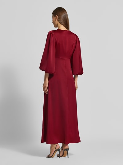 Frauenmodel trägt Cocktailkleid mit Knotendetail und V-Ausschnitt Modell 'THEA' von YAS, A-Linie, Maxikleid, Material-Mix, Ganzkörperansicht Rückansicht.