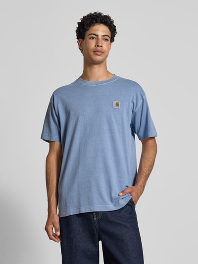 Männermodel trägt T-Shirt mit Label-Detail Modell 'Nelson' von Carhartt Work In Progress in Hellblau, reine Baumwolle, Relaxed Fit, Ganzkörperansicht von vorne.
