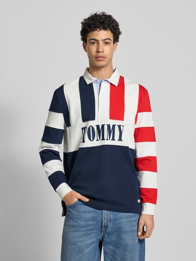 Männermodel trägt Relaxed Fit Poloshirt aus reiner Baumwolle von Tommy Jeans in Optik: Unifarben, mehrfarbig mit Label-Schriftzug, Ganzkörperansicht von vorne.