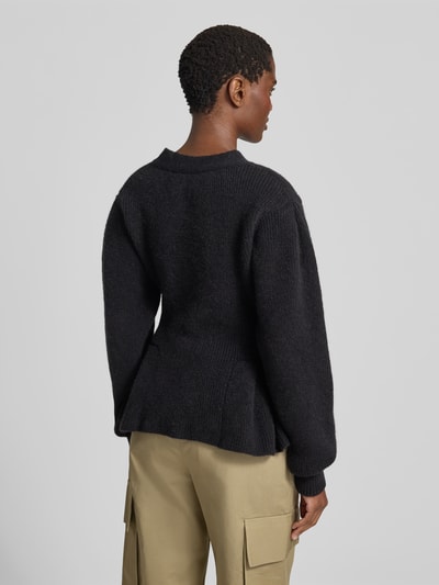 Frauenmodel trägt Relaxed Fit Cardigan aus Alpaka-Mix von ROTATE in Schwarz, mit Strick-Optik, Volant-Saum, Woll-Anteil, Ganzkörperansicht Rückansicht.
