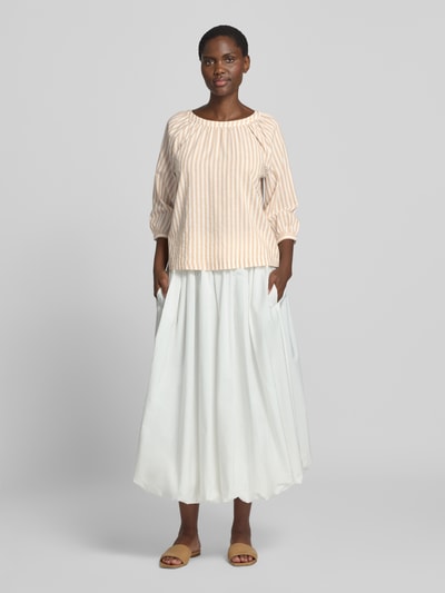 Frauenmodel trägt Loose Fit Kurzarmbluse aus Viskose-Baumwoll-Mix von s.Oliver RED LABEL in Beige mit Streifen, kombiniert mit weißem Rock, Ganzkörperansicht von vorne.