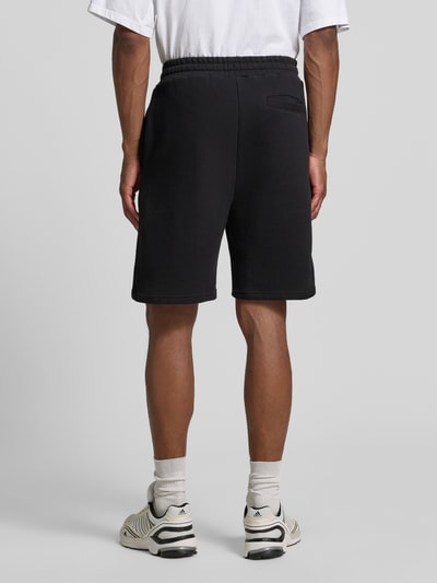 Männermodel trägt schwarze Regular Fit Shorts mit Tunnelzug von COLUCCI aus reiner Baumwolle, Label-Stitching, Rückansicht Ganzkörperansicht.
