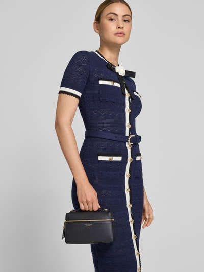 Frauenmodel trägt Kosmetik-Tasche mit Logo-Detail von Tory Burch, schwarz, goldene Details, abnehmbarer Schulterriemen, Hauptfach mit Zweiwege-Reißverschluss, Logo-Print, Logo-Prägung, strukturierte Oberfläche, Maße ca. 19 cm Breite, 13 cm Länge, 6 cm Tiefe, Nahaufnahme Oberkörper.