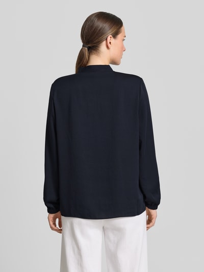 Frauenmodel trägt Bluse mit V-Ausschnitt und Label-Detail von Marc Cain in Schwarz, Loose-Fit, elastische Ärmelabschlüsse, Rückenlänge 46 cm, Ärmellänge 60 cm bei Größe 36, Ganzkörperansicht Rückansicht.