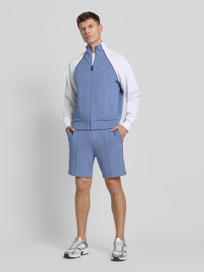 Männermodel trägt Regular Fit sweatjack uit katoenmix model 'JOIN SKAZ' van BOSS in tweekleurige look met ritssluiting, labelstitching, opstaande kraag, lange mouwen met geribde mouwboord, zij-steekzakken en piqué sweat-materiaal, ganzkörperansicht van voren.